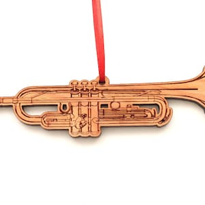 May include: A wooden ornament shaped like a trumpet. The ornament is detailed with the internal workings of the instrument. It has a red ribbon attached for hanging.