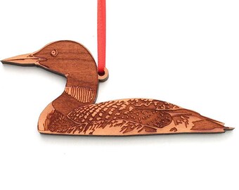 Könnte beinhalten: Ein Holz-Anhänger in Form eines  Seetauchers, einer Art Tauchvogel, mit einem roten Band. Der Seetaucher ist aus braunem Holz geschnitzt und hat ein detailliertes Design.