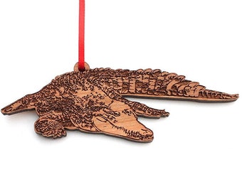 May include: A wooden Christmas ornament shaped like a crocodile with a red ribbon attached. The ornament is detailed with a woodgrain pattern and a realistic depiction of the crocodile's scales.