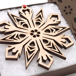 May include: A wooden snowflake ornament with intricate cutouts, displayed in a brown box with white lining.