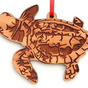 May include: A wooden sea turtle ornament with a detailed carved design. The ornament is made of light brown wood and has a red ribbon attached for hanging.