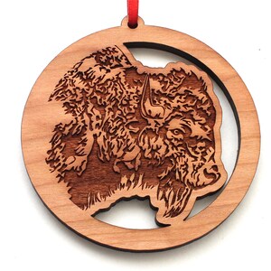 May include: A wooden ornament featuring a detailed laser-cut design of a bison head. The ornament is circular and has a red ribbon attached.