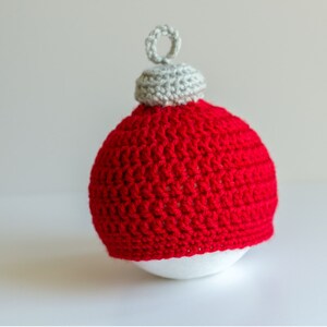 May include: A red crocheted Christmas ornament with a white crocheted top. The ornament is sitting on a white surface.