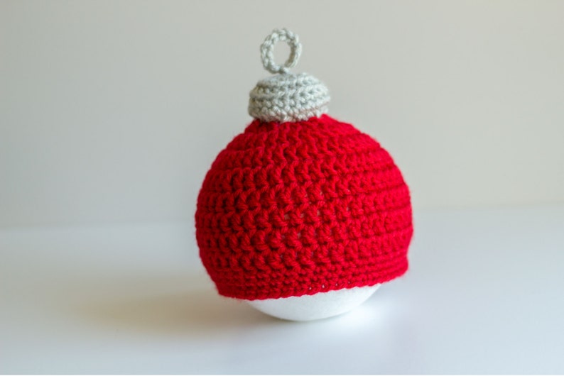 May include: A red crocheted Christmas ornament with a white crocheted top. The ornament is sitting on a white surface.