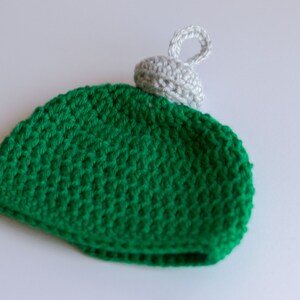 May include: Green crocheted ornament with a white crocheted top and a loop for hanging.