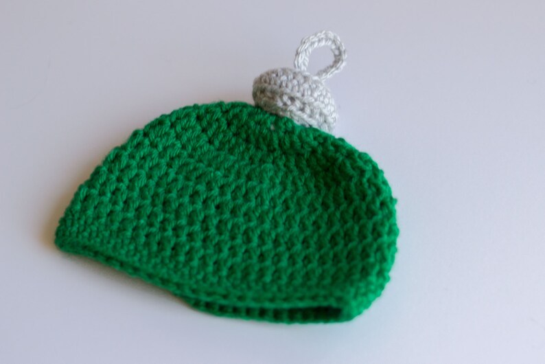 May include: Green crocheted ornament with a white crocheted top and a loop for hanging.