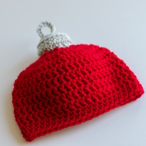 May include: A red and gray crocheted ornament shaped like a Christmas tree ornament.