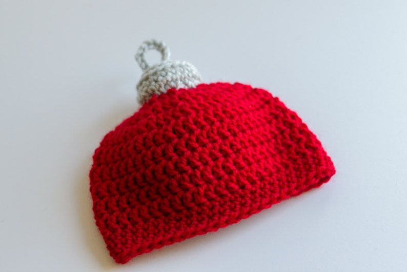 May include: A red and gray crocheted ornament shaped like a Christmas tree ornament.