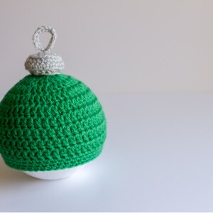 May include: A green crocheted Christmas ornament with a white crocheted top and a loop for hanging.