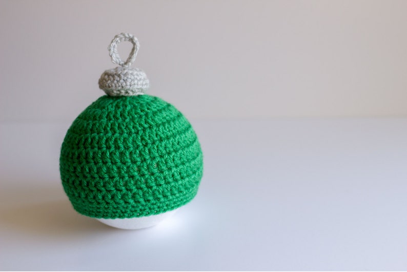 May include: A green crocheted Christmas ornament with a white crocheted top and a loop for hanging.