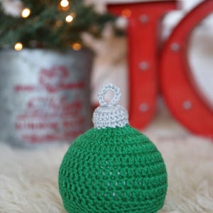 May include: A green and gray crocheted Christmas ornament shaped like a ball with a loop at the top.