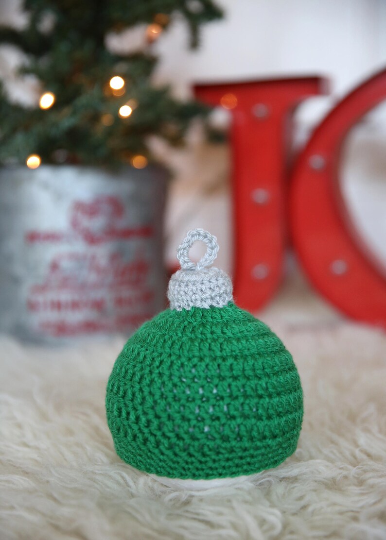 May include: A green and gray crocheted Christmas ornament shaped like a ball with a loop at the top.