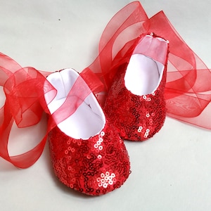 Könnte beinhalten: Ein Paar rote, mit Pailletten besetzte Babyschuhe mit einem roten Satinband.