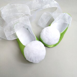 May include: A pair of green satin baby shoes with white pom-poms and a white tulle ribbon.