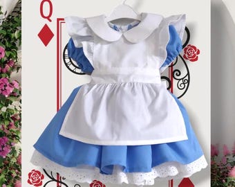 May include: A white and blue dress with a white apron and a lace trim. The dress has a Peter Pan collar and short puffed sleeves. The dress is a costume for a child.