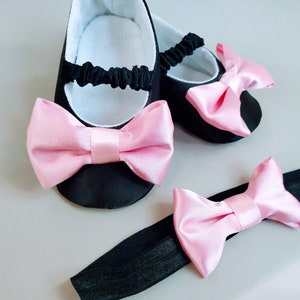 Peut inclure: Une paire de chaussures de b&eacute;b&eacute; noires avec des n&oelig;uds en satin rose. Un bandeau assorti avec un n&oelig;ud en satin rose est &eacute;galement inclus.