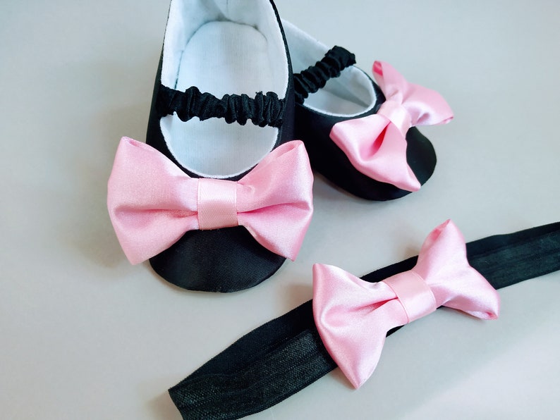 Peut inclure: Une paire de chaussures de b&eacute;b&eacute; noires avec des n&oelig;uds en satin rose. Un bandeau assorti avec un n&oelig;ud en satin rose est &eacute;galement inclus.