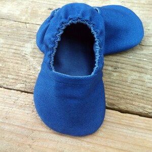 Op de afbeelding: Een paar felblauwe babyschoentjes van zachte stof. De schoenen hebben een elastische opening en een ronde neus. Ze liggen op een lichtbruin houten oppervlak.