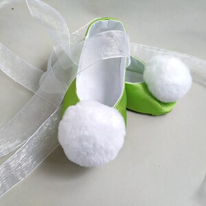 May include: A pair of green satin baby shoes with white pom-poms and white satin ribbon ties.