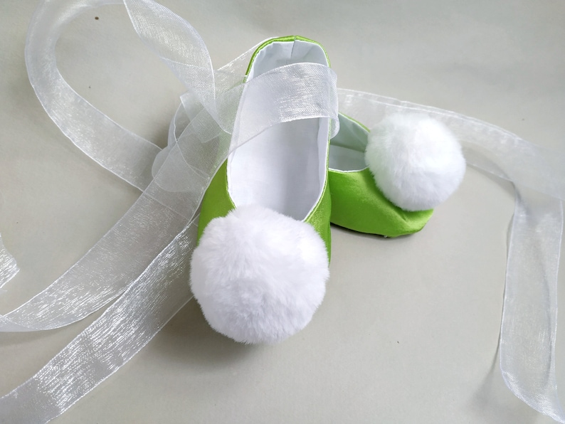 May include: A pair of green satin baby shoes with white pom-poms and white satin ribbon ties.