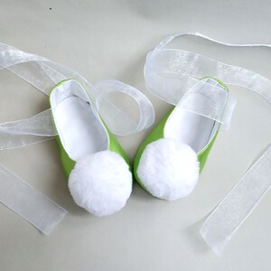 May include: A pair of green satin ballet slippers with white pom-poms and white satin ribbon ties.