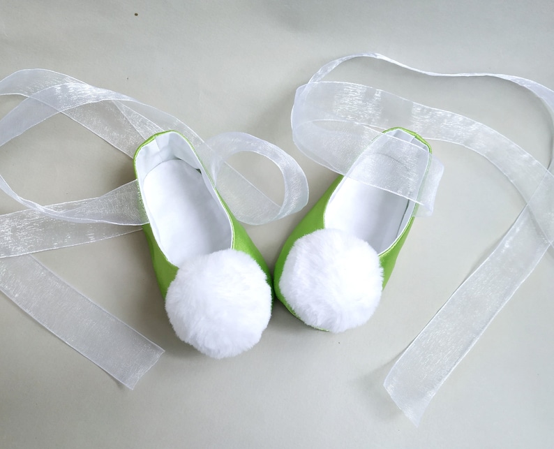 May include: A pair of green satin ballet slippers with white pom-poms and white satin ribbon ties.