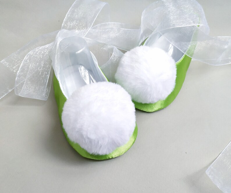 May include: A pair of green satin ballet slippers with white fluffy pom-poms and white sheer ribbon ties.