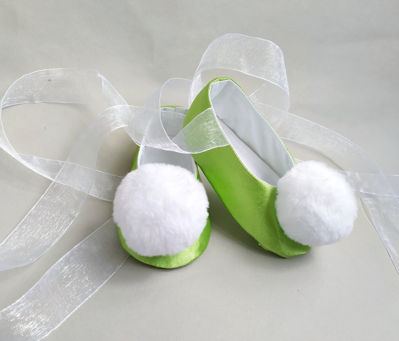 May include: A pair of lime green satin ballet slippers with white pom-poms and white satin ribbon ties.