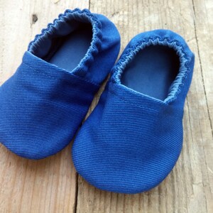 Op de afbeelding: Een paar blauwe babyschoentjes van geribbelde stof. De schoentjes hebben een zachte, elastische opening en een eenvoudig, afgerond ontwerp. Deze schoentjes zijn ontworpen voor baby's en peuters.