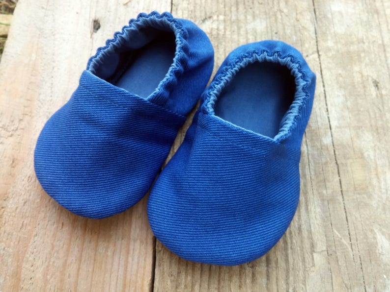 Op de afbeelding: Een paar blauwe babyschoentjes van geribbelde stof. De schoentjes hebben een zachte, elastische opening en een eenvoudig, afgerond ontwerp. Deze schoentjes zijn ontworpen voor baby's en peuters.