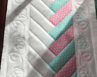 May include: A rectangular quilted table runner featuring a central herringbone pattern of alternating white, pink polka dot, and mint green polka dot fabric strips. The piece is framed by white borders with machine-stitched floral vine motifs.