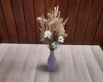 Può includere: Un mazzo di fiori secchi in un vaso lilla chiaro. Il mazzo comprende erbe secche, boccioli di cotone e teste di fiori secchi.
