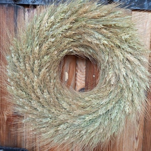 May include: A wreath made of dried wheat stalks, arranged in a circular shape. The wreath is a light beige color and has a rustic, natural look.