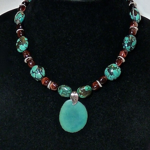 May include: A turquoise and brown beaded necklace with a large turquoise pendant. The necklace is made of round beads and has a silver clasp.