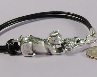 May include: A silver cat charm bracelet with a black leather cord. The cat charm is holding a ball of yarn in its paws.