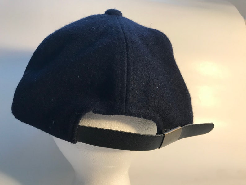 Puede incluir: Una gorra de b&eacute;isbol azul oscuro con una correa ajustable negra y una hebilla plateada.