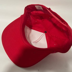 May include: Red baseball cap with a white mesh back and a black button on the top. The cap is turned inside out, showing the white lining.