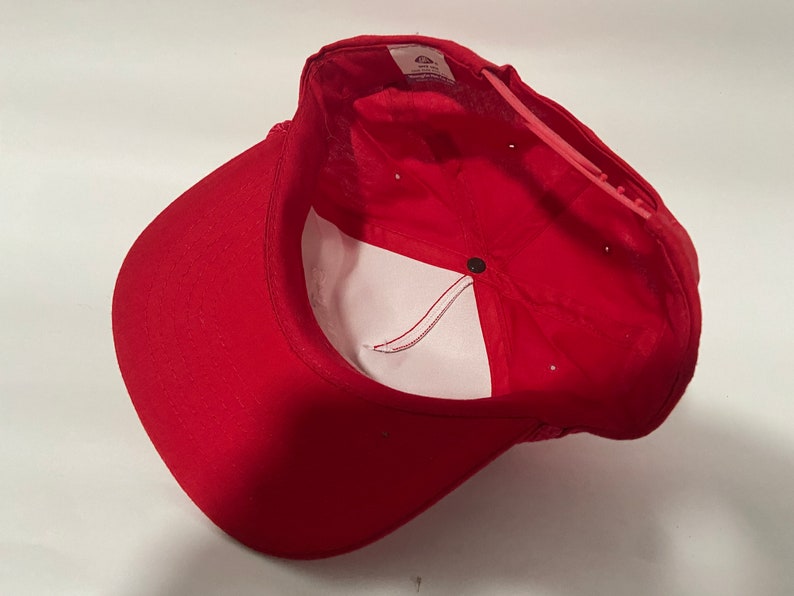 May include: Red baseball cap with a white mesh back and a black button on the top. The cap is turned inside out, showing the white lining.