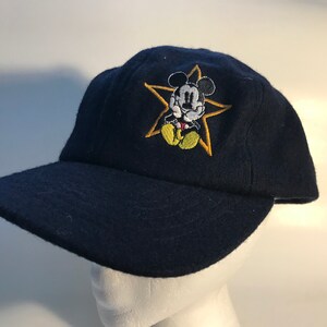 Puede incluir: Una gorra de b&eacute;isbol azul marino con una estrella amarilla y un dibujo animado de Mickey Mouse bordado en la parte delantera.