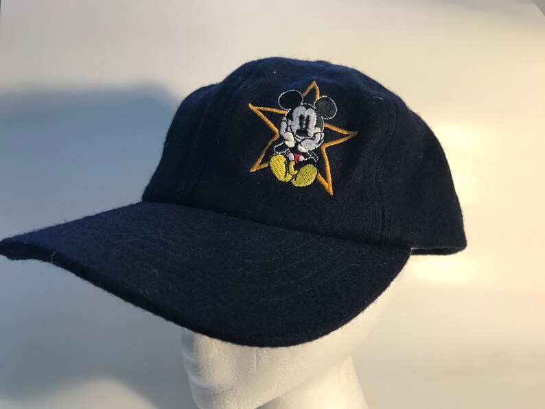 Puede incluir: Una gorra de b&eacute;isbol azul marino con una estrella amarilla y un dibujo animado de Mickey Mouse bordado en la parte delantera.