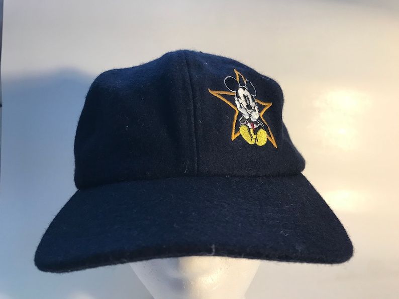Puede incluir: Una gorra de b&eacute;isbol azul marino con una estrella amarilla y Mickey Mouse bordados en la parte delantera.