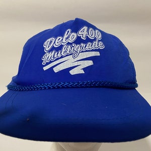 Könnte beinhalten: Eine blaue Baseballkappe mit einem weißen Logo, auf dem "Delo 400 Multigrade" steht.