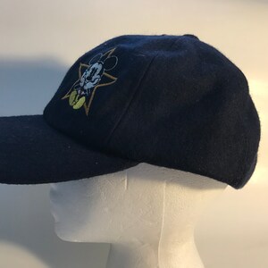 Puede incluir: Una gorra de b&eacute;isbol azul marino con una estrella dorada y una imagen bordada de Mickey Mouse.