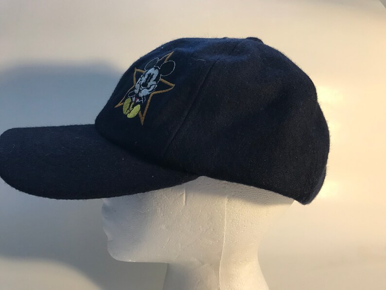 Puede incluir: Una gorra de b&eacute;isbol azul marino con una estrella dorada y una imagen bordada de Mickey Mouse.