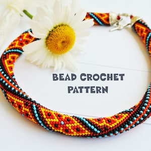Op de afbeelding: Een kralen gehaakte ketting met een geometrisch patroon in tinten rood, oranje, geel, zwart en blauw. De ketting ligt op een wit oppervlak met een witte madeliefje.