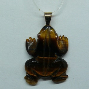 May include: A gold chain necklace with a tiger's eye frog pendant. The frog has red gemstone eyes.