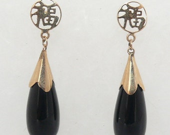 May include: A pair of gold earrings with black teardrop-shaped stones. The earrings feature a circular charm with Chinese characters.