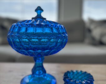 Op de afbeelding: Een levendige blauwe glazen bonbonnière met deksel en een kleine, bijpassende asbak. De bonbonnière heeft een voet en een oppervlak met textuur en patronen. De asbak is rond met een vergelijkbaar textuurontwerp.