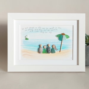 May include: A framed artwork featuring a beach scene with a family of five figures made from sea glass, a green and blue umbrella, and the quote "The best things in life are the people we love, the places we've been, and the memories we've made along the way."