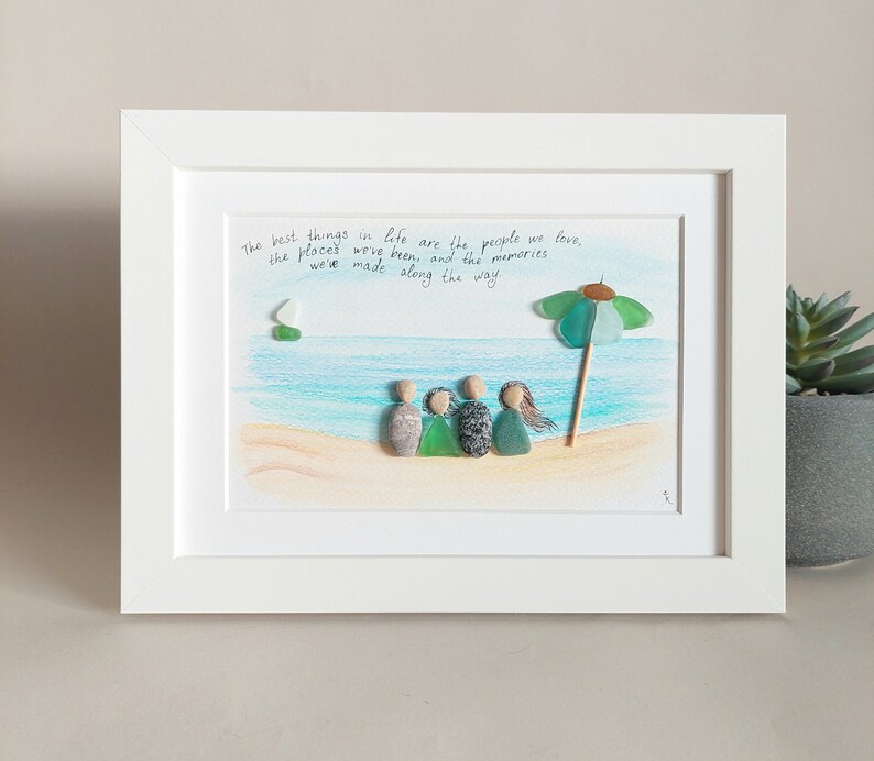 May include: A framed artwork featuring a beach scene with a family of five figures made from sea glass, a green and blue umbrella, and the quote "The best things in life are the people we love, the places we've been, and the memories we've made along the way."